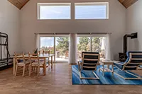 Outdoor patio area with stone columns supporting a wooden deck overhead. There is a concrete countertop with two stools, surrounded by potted plants. The shaded space underneath the deck offers a relaxing retreat, perfect for vacation rentals in Humboldt. A gray house with a window is visible in the background.