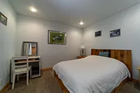 A small, modern bedroom in Humboldt with a gray color scheme features a double bed with a wooden headboard and white bedding. A desk with a mirror and chair is positioned on one side. The walls are adorned with framed pictures, and the room is illuminated by recessed lighting, perfect for vacation rentals.